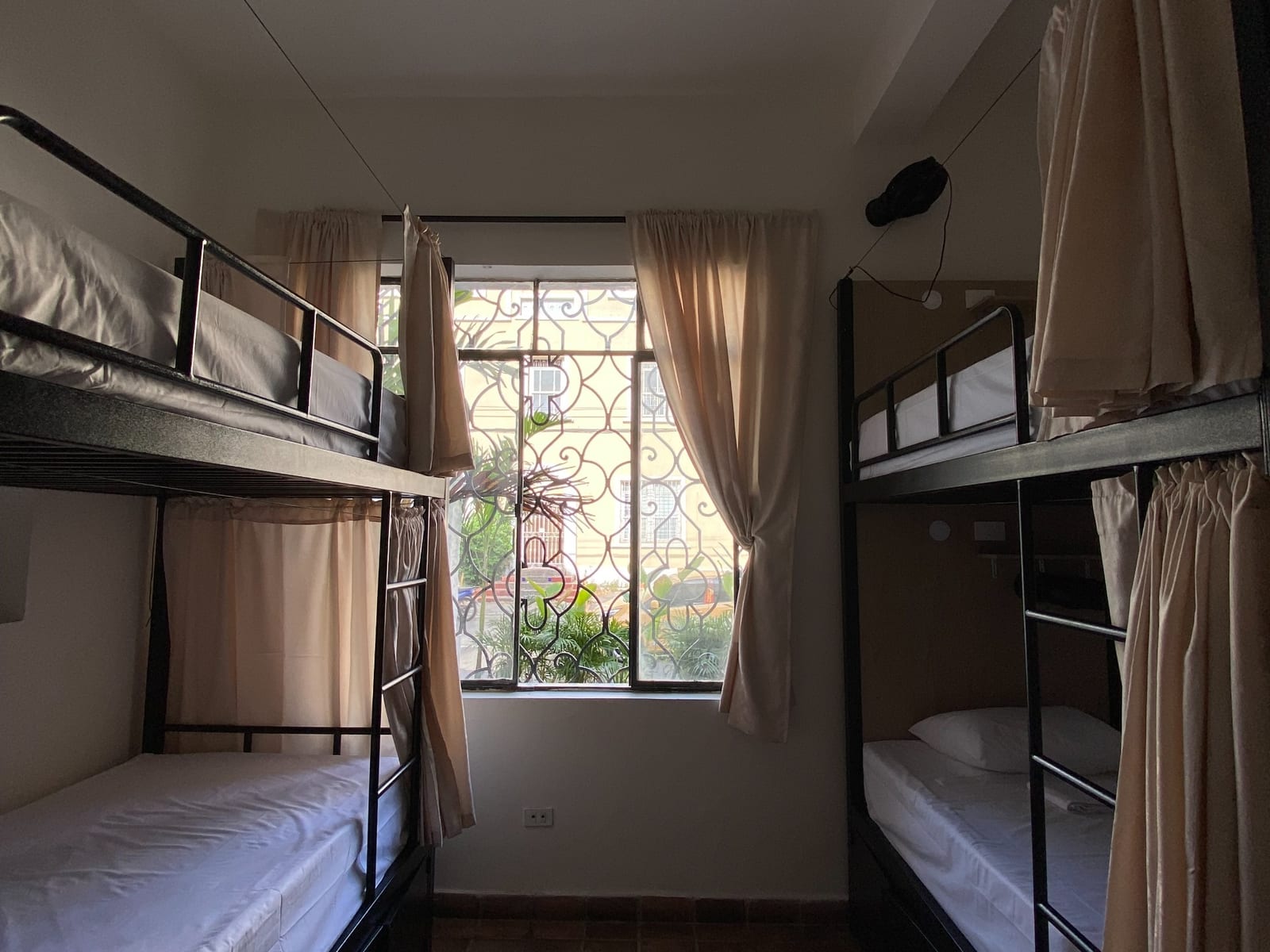 A six-bed mixed dorm: the window end of the room, morning light through the ironwork onto the terracotta floor.